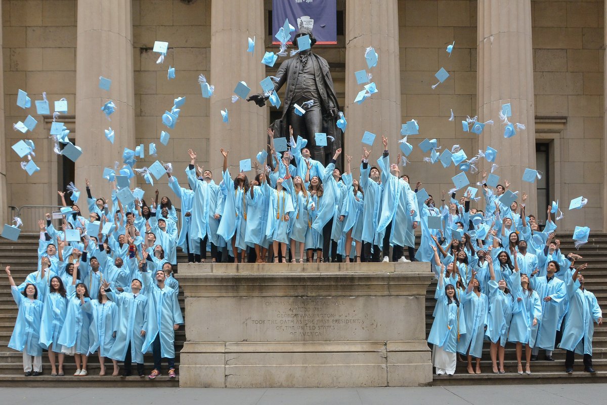 Graduates throw their caps up in front of Federal Hall